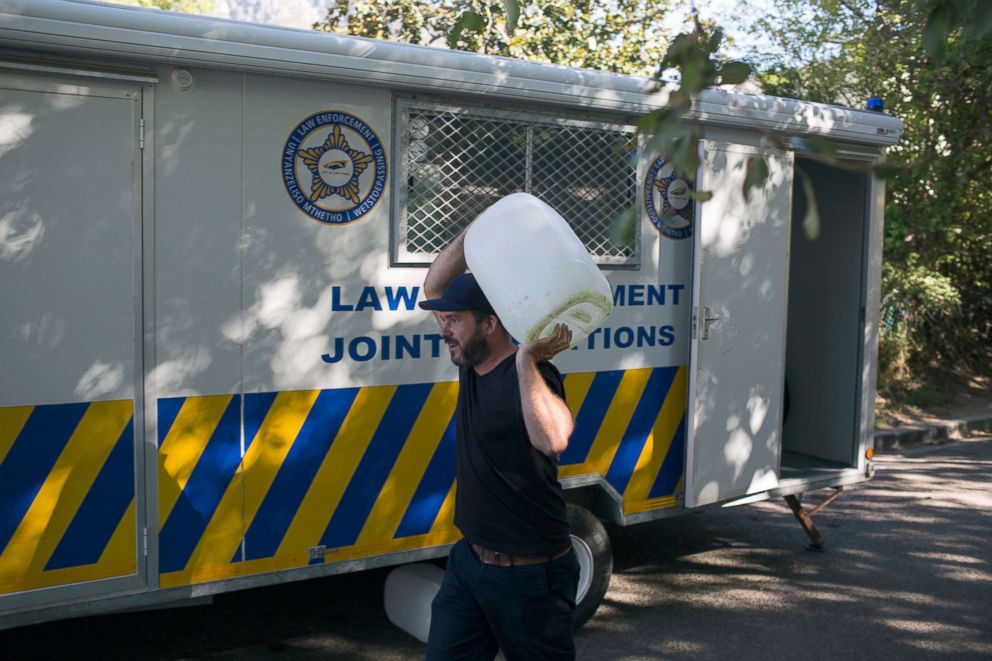 PHOTO: A man carrying a container of water passes a police trailer parked outside a source for natural spring water in Cape Town, Feb. 1, 2018.