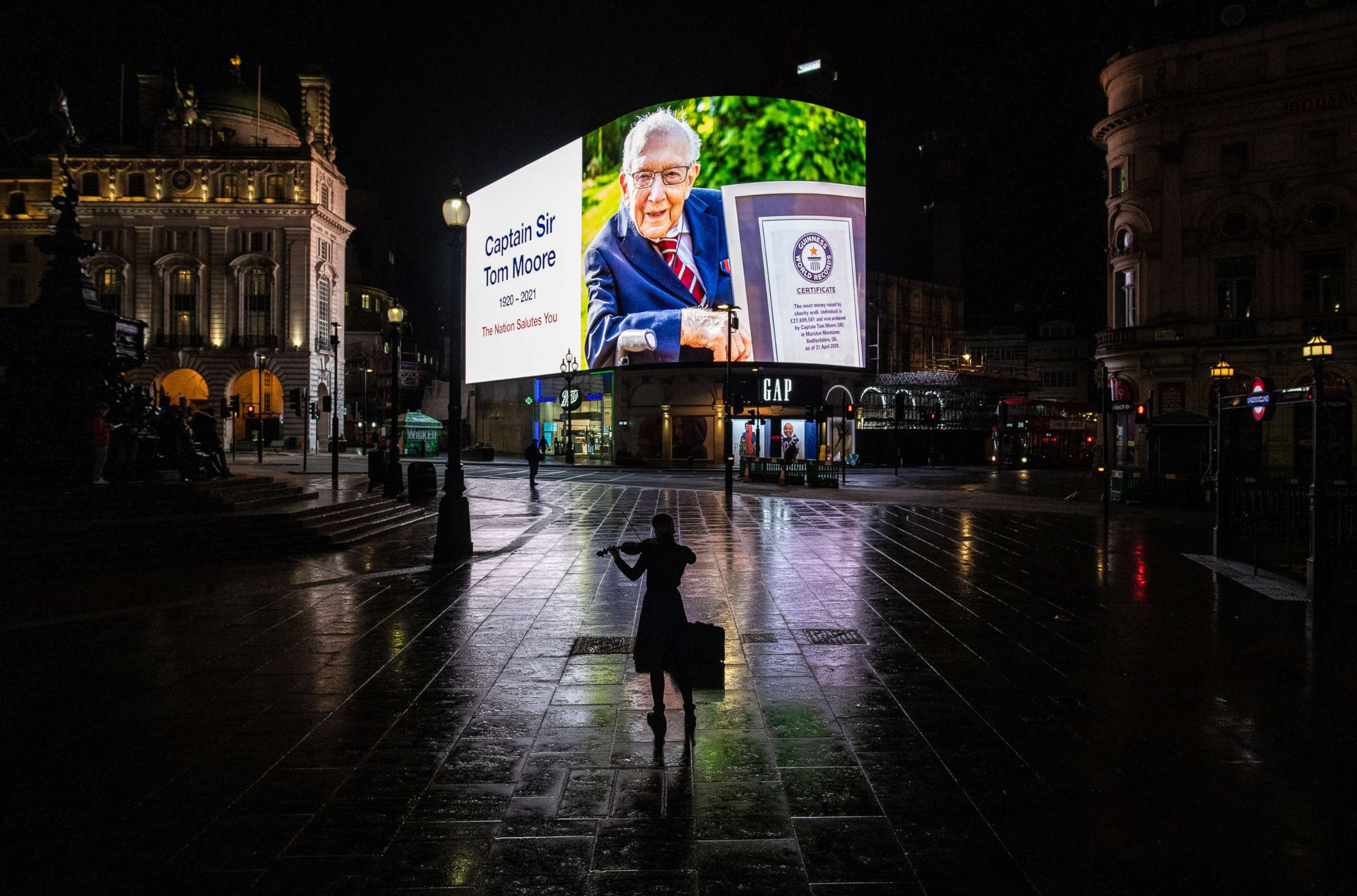 PHOTO: A violinist plays in front of a tribute to Captain Sir Tom Moore that is displayed at Piccadilly Circus shortly after it was announced that he has died on Feb. 2, 2021 in London.