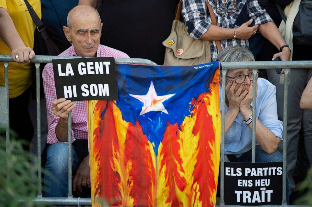 PHOTO: Two people hold signs reading in Catalan "We the people remain" and "Political parties have betrayed us" next to a Catalan pro-independence Estelada flag in Barcelona on Oct. 1, 2022.