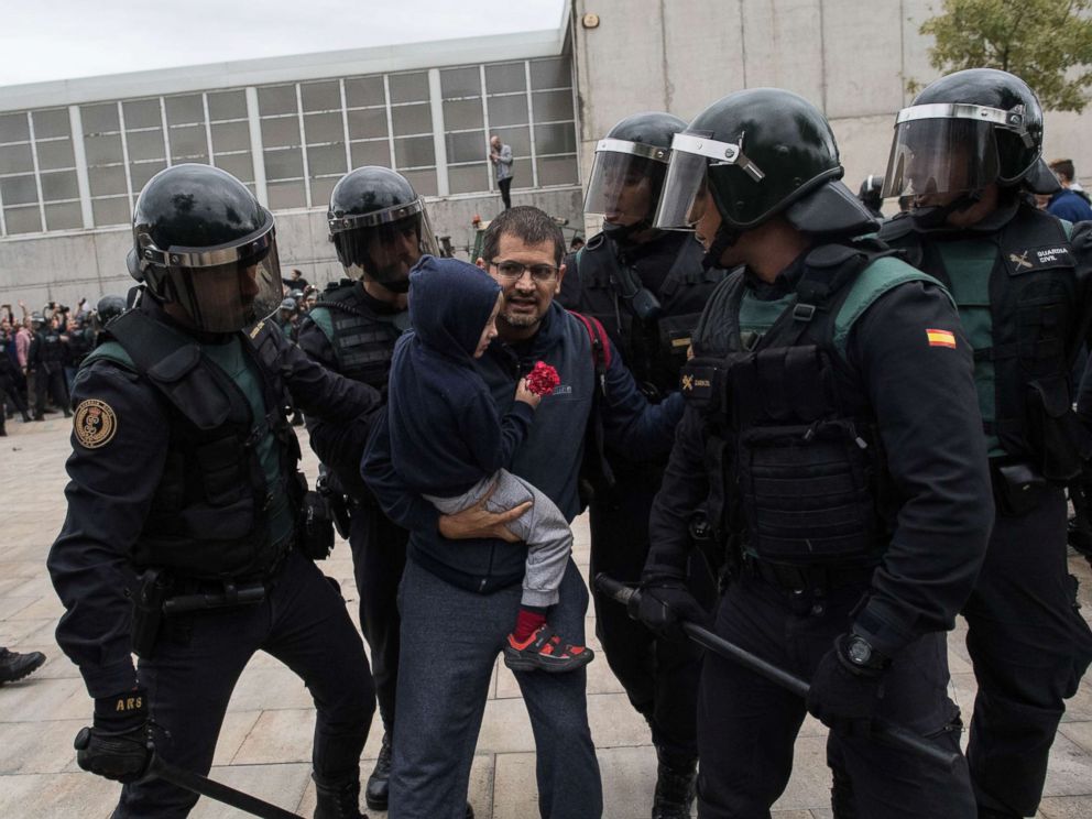 PHOTO: A man and a child holding a red flower run from the police as they move in on the crowds, Oct. 1, 2017 in Sant Julia de Ramis, Spain.