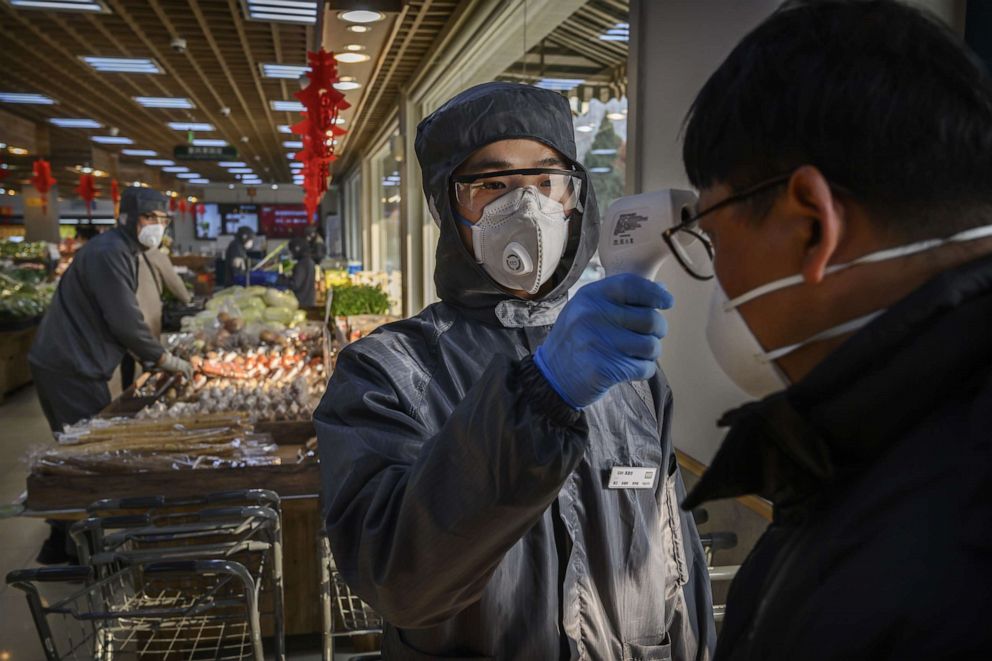 PHOTO: A Chinese worker checks the temperature of a customer amid a coronavirus outbreak as he wears a protective suit and mask at a supermarket in Beijing, China, on Feb. 11, 2020.