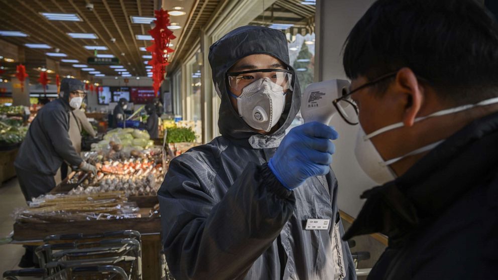 PHOTO: A worker checks the temperature of a customer amid a coronavirus outbreak as he wears a protective suit and mask at a supermarket in Beijing, China, on Feb. 11, 2020.