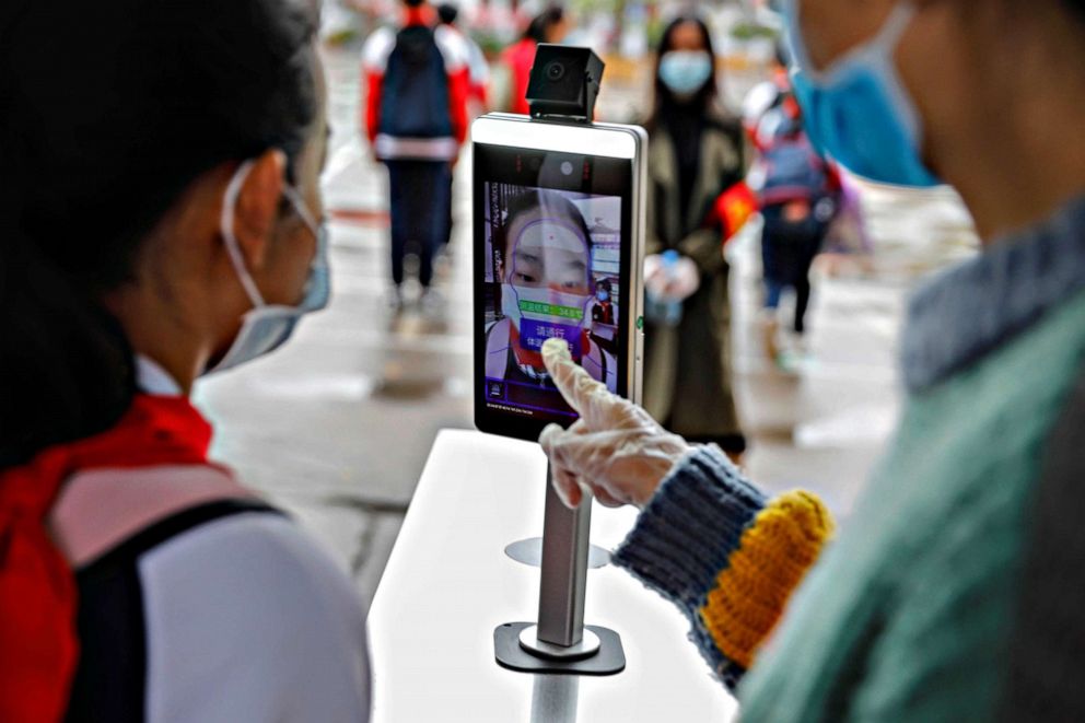 PHOTO: A staff member guides a student to check her body temperature with a thermal scanner before entering an elementary school in Pingdingshan City, in China's central Henan province, on May 8, 2020.