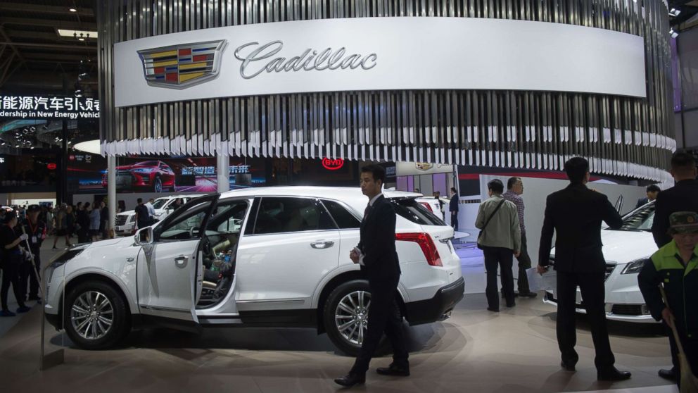 People walk through the Cadillac car display during the Beijing Auto Show in Beijing on April 25, 2018.