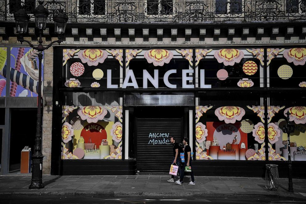 PHOTO: Two men carry grocery bags as they walk past a closed shop bearing graffiti that reads "old world" in Paris on April 21, 2020, on the thirty-sixth day of France's nationwide lockdown aimed at curbing the spread of the novel coronavirus.