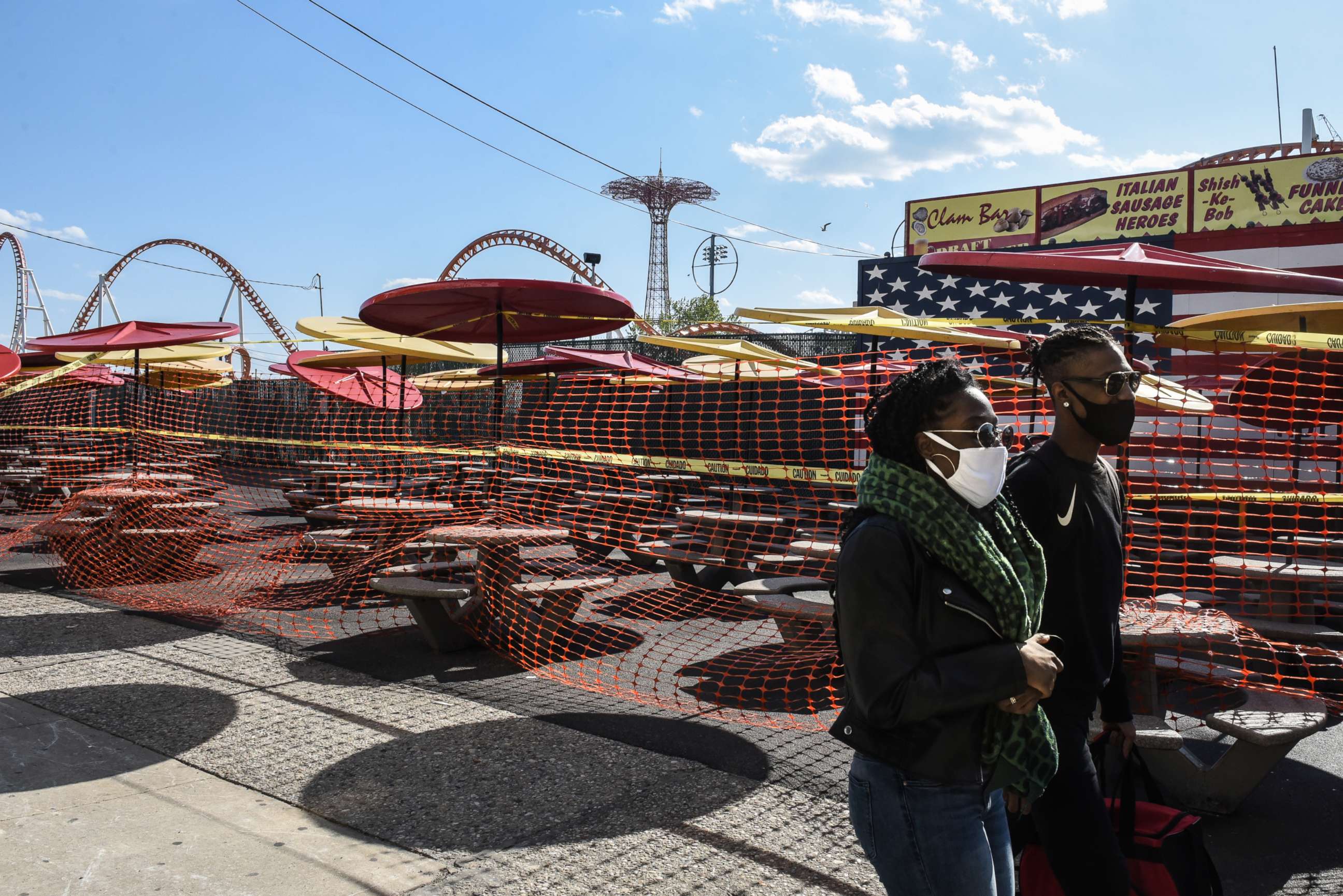 PHOTO: People with masks walk past a closed outdoor seating area for Nathan's restaurant, on May 13, 2020, in the Coney Island neighborhood of Brooklyn, New York.