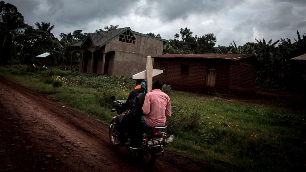 PHOTO: People carrying a cross for a grave, ride a motorbike along the road linking Mangina to Beni in the North Kivu province of the Democratic Republic of Congo.