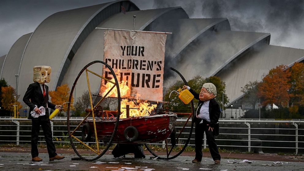 PHOTO: Activists from Ocean Rebellion dressed as Boris Johnson and an Oilhead, set light to the sail of a small boat during a demonstration near the COP26 site, Oct. 27, 2021, in Glasgow, Scotland. 
