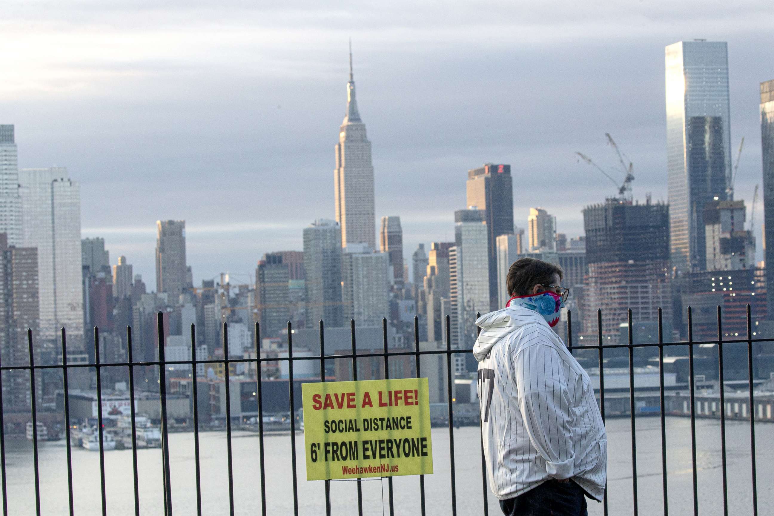 PHOTO: A man wears a face mask as he walks with the Manhattan skyline behind him, April 6, 2020, as seen from Weehawken, New Jersey.