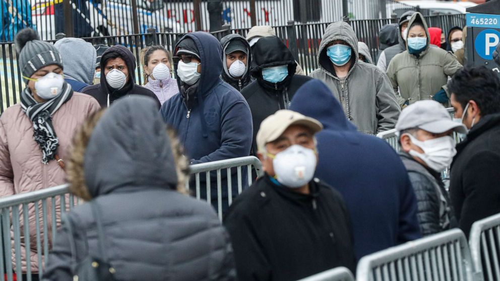 PHOTO: Patients wear personal protective equipment while maintaining social distancing as they wait in line for a COVID-19 test at Elmhurst Hospital Center, March 25, 2020, in New York.