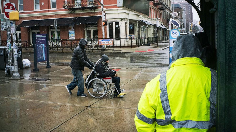 PHOTO: A man is pushed in his wheelchair to the Path train station where service operates on a weekend schedule due to the coronavirus outbreak, March 23, 2020, in Hoboken, N.J. 