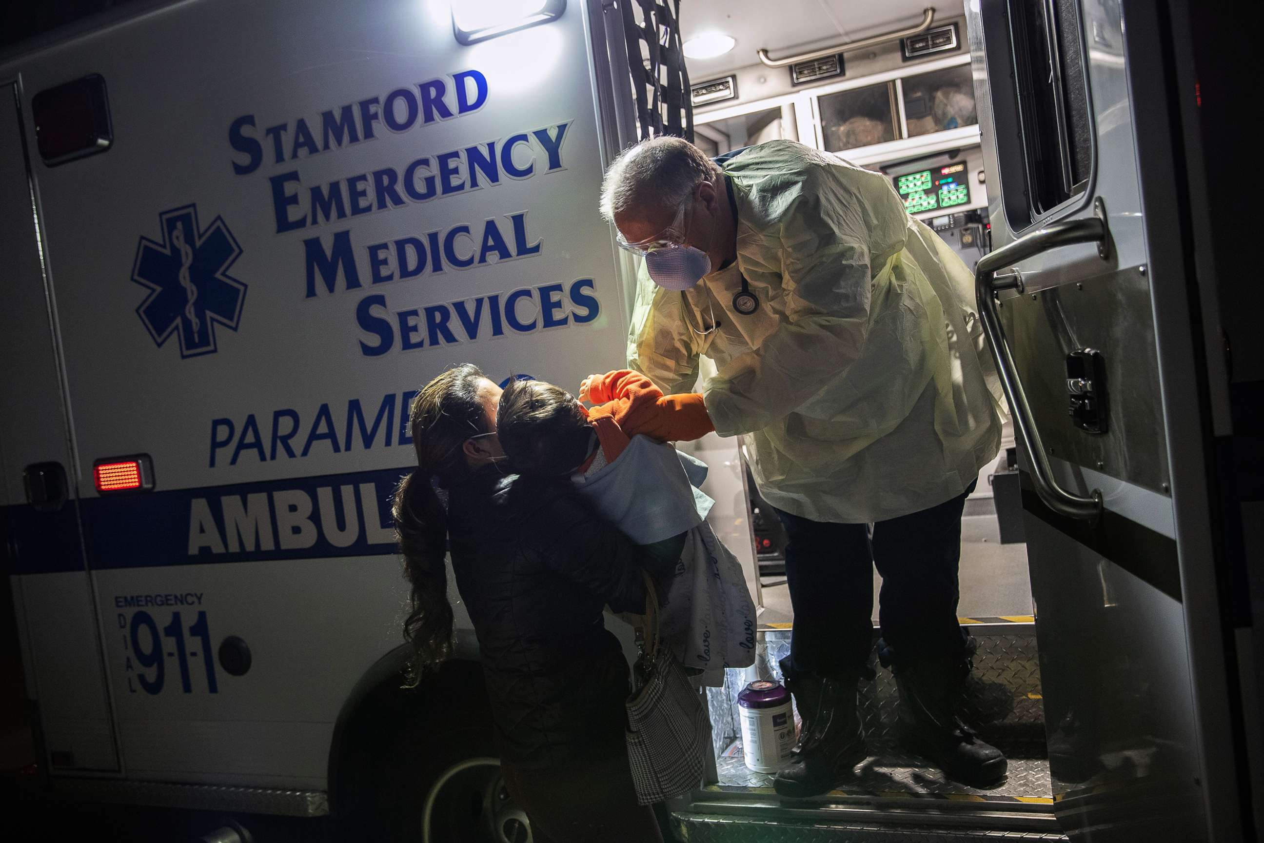 PHOTO: Paramedic Randy Lilly, wearing personal protection equipment (PPE), hands a 10-month-old boy with fever to his mother after upon arriving together by ambulance to Stamford Hospital, April 4, 2020, in Stamford, Conn. 