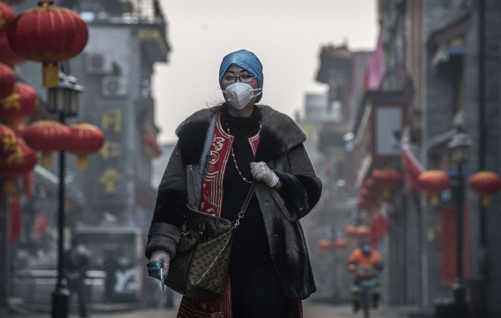 PHOTO: A Chinese woman wears a protective mask and gloves as she walks in a nearly empty and shuttered commercial street on Feb. 12, 2020 in Beijing.