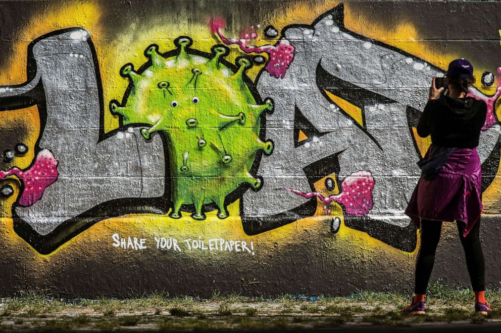 PHOTO: A woman takes photographs of graffiti reading 'Share your toilet paper!' in Vienna, Austria, March 27, 2020.