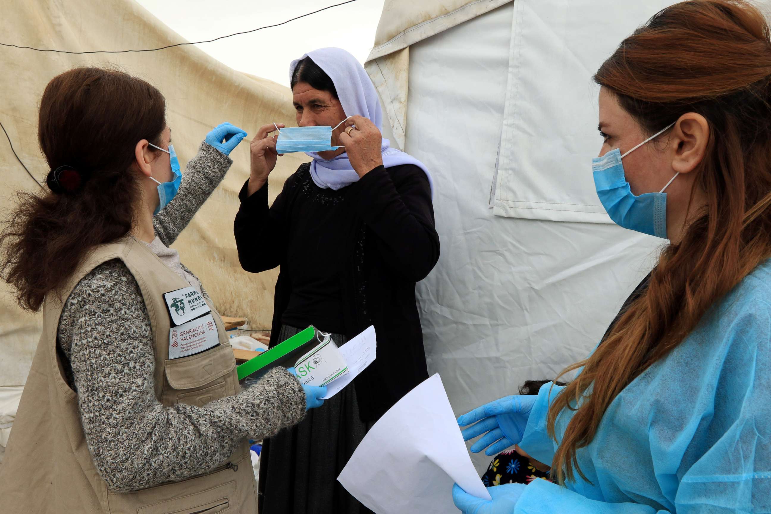 PHOTO: A member of medical staff, assists a Yazidi displaced woman to wear a protective face mask, following the coronavirus outbreak, at the Sharya camp in Duhok, Iraq, March 7, 2020.