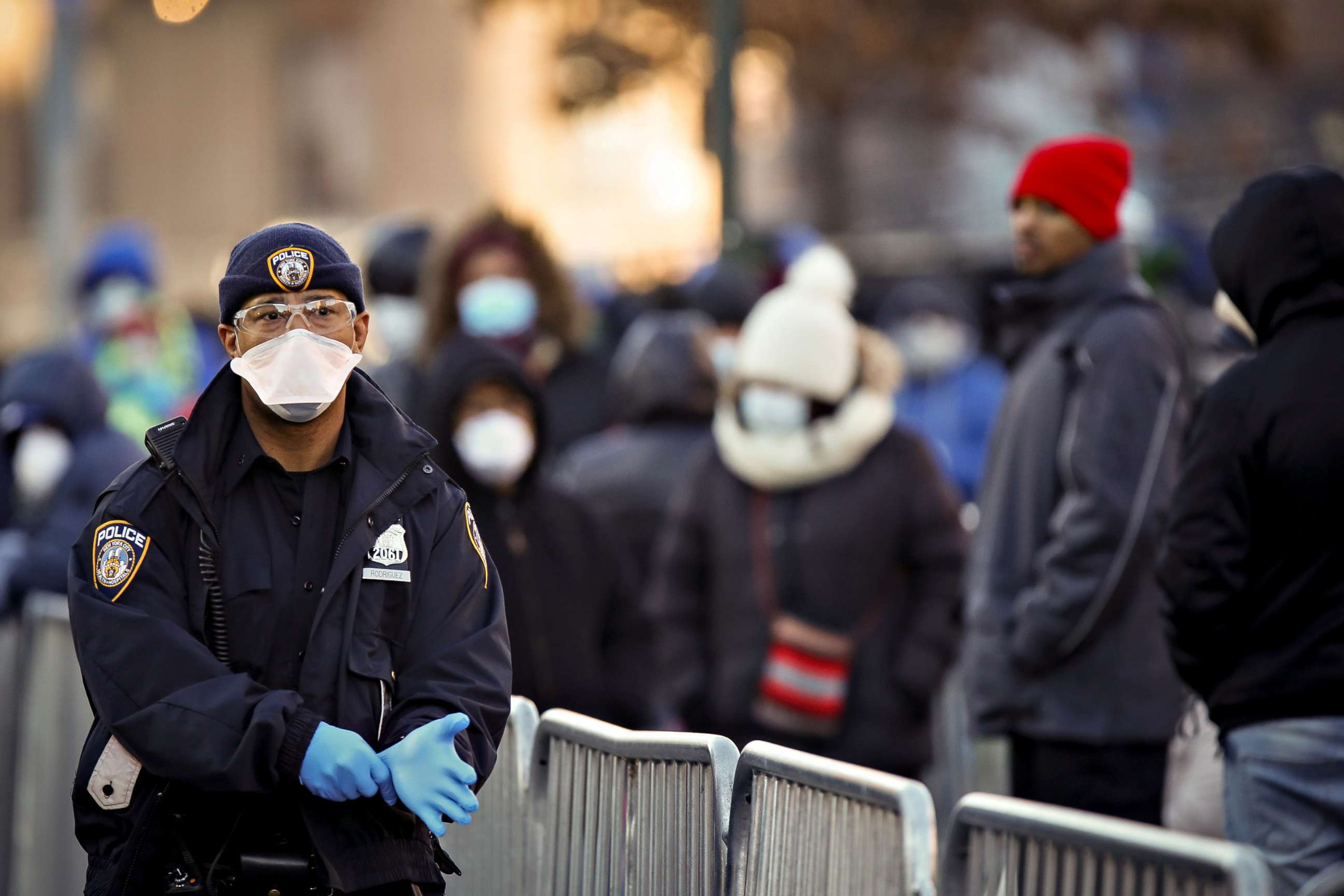 PHOTO: A New York City Police officer puts on gloves as people wait in line to be tested for COVID-19, outside Elmhurst Hospital Center in the Queens borough of New York City, March 26, 2020.