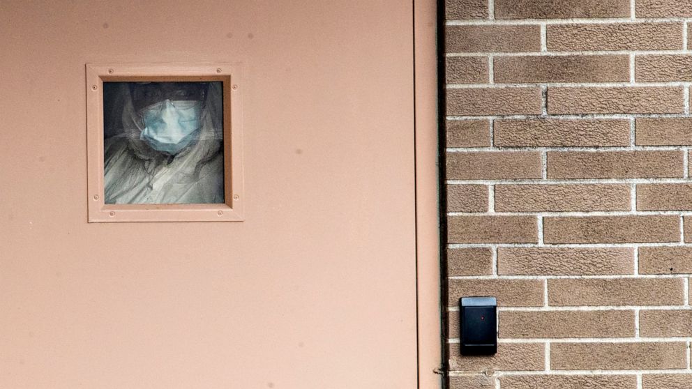 PHOTO: A medical person looks out the window of a back door at the Wycoff Heights Medical Center at refrigerated containers parked outside, April 2, 2020, in the Brooklyn, New York.