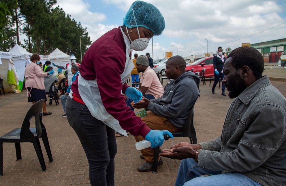 PHOTO: A health worker sprays sanitizer on a man's hands as people undergo screening and testing for the novel coronavirus in Lenasia, south of Johannesburg, South Africa, on April 8, 2020.