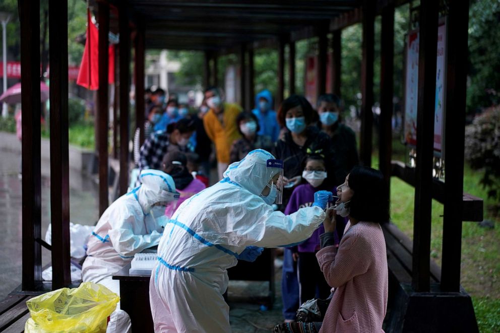 PHOTO: A medical worker in a protective suit conducts a nucleic acid testing for COVID-19 on a resident as people wearing face masks queue behind for testings at a residential compound in Wuhan in China's central Hubei province on May 14, 2020.