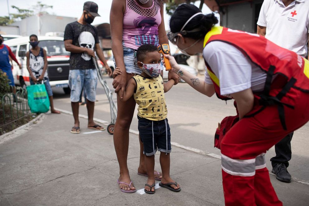 PHOTO: A member of the Red Cross checks the temperature of a child at the CEASA, Rio de Janeiro's main wholesale market, amid the new coronavirus pandemic in Rio de Janeiro, Tuesday, June 23, 2020.