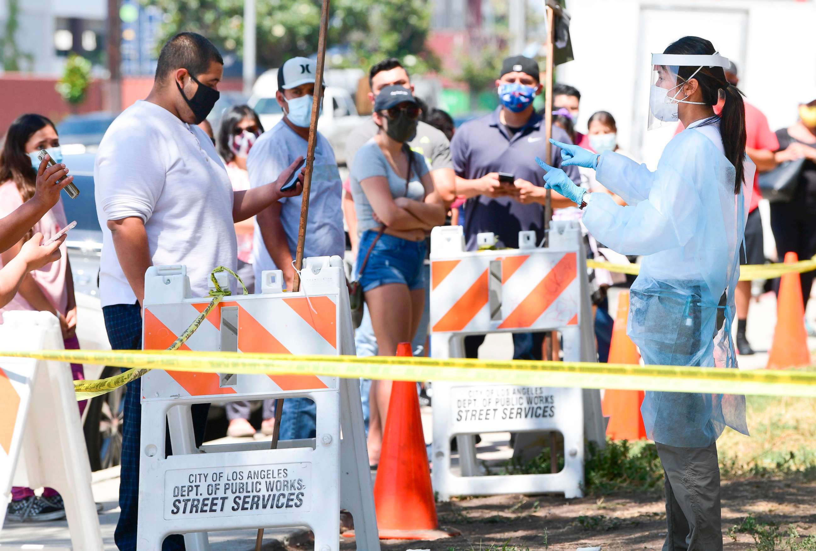 PHOTO: A COVID-19 test site volunteer speaks with people waiting in line at a walk-in coronavirus test site in Los Angeles, July 10, 2020.