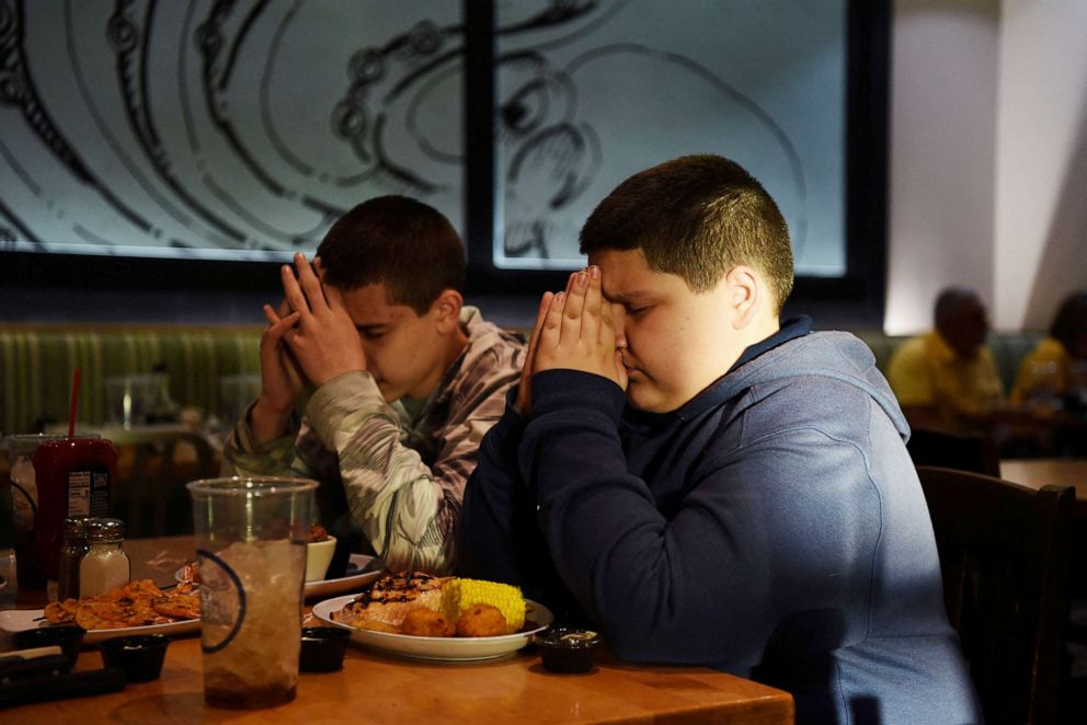 PHOTO: Brothers Julius Garza, 14, and Aidan Garza, 12, say a prayer in honor of their father, David Garza, who died from the coronavirus disease in December 2020, while out to eat in Converse, Texas, March 30, 2022.