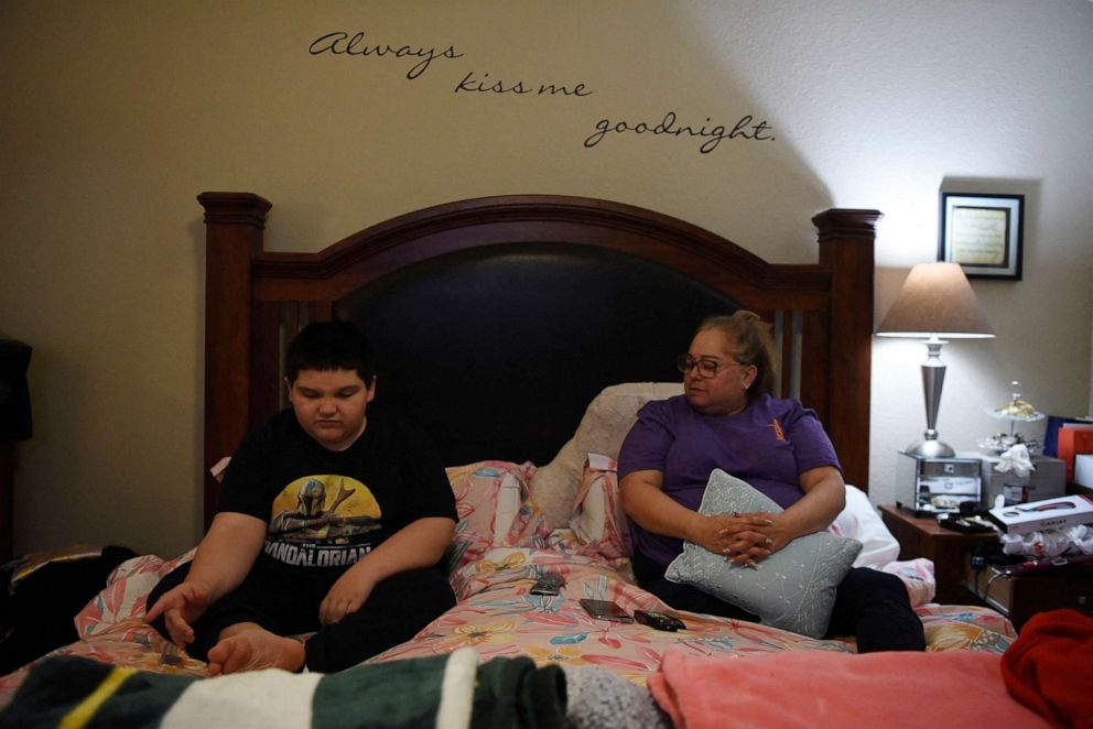 PHOTO: Aidan Garza, 12, and his mother, Margaret Garza, watch television in Margaret's bedroom in Converse, Texas, Feb. 27, 2022.