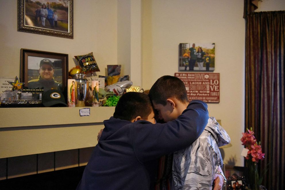 PHOTO: Aidan Garza, 12, (L) Julius Garza, 14, (R) and Margaret Garza (C) pray together next to their father's urn, which they call "the vessel," in Converse, Texas, March 30, 2022.