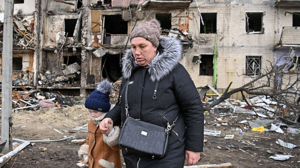 PHOTO: A woman with a child walk in front of a damaged residential building at Koshytsa Street, a suburb of the Ukrainian capital Kyiv, on Feb. 25, 2022. 