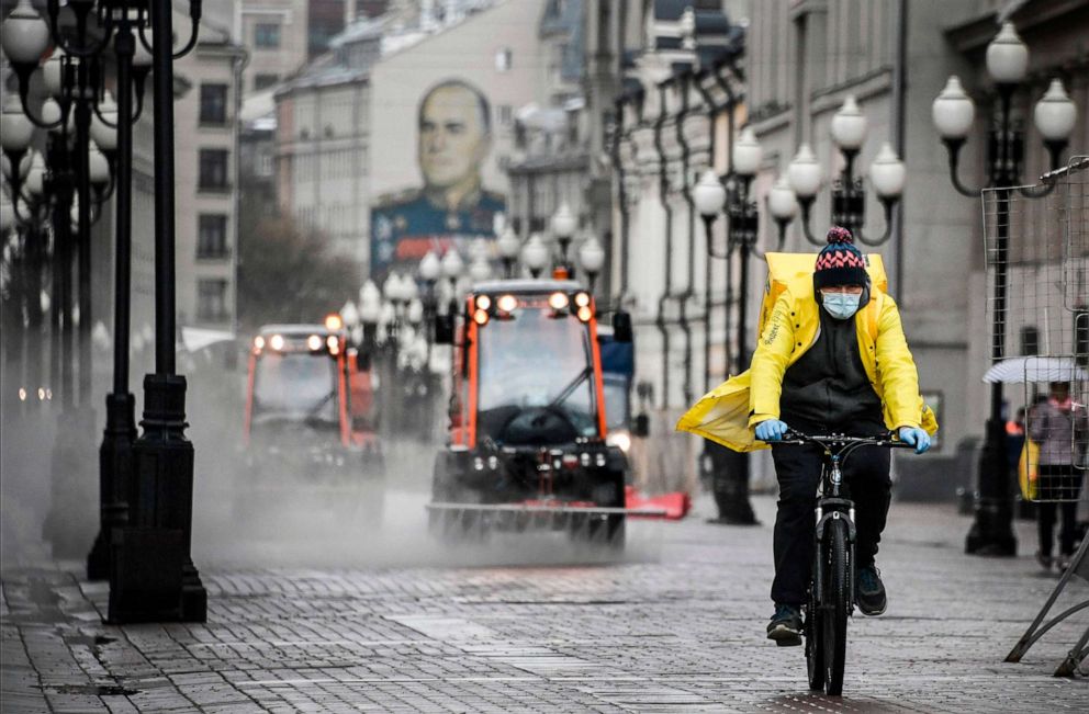 PHOTO: A food delivery courier cycles along pedestrian Arbat street as municipal vehicles clean and disinfect the area, in downtown Moscow, Russia, on April 14, 2020.