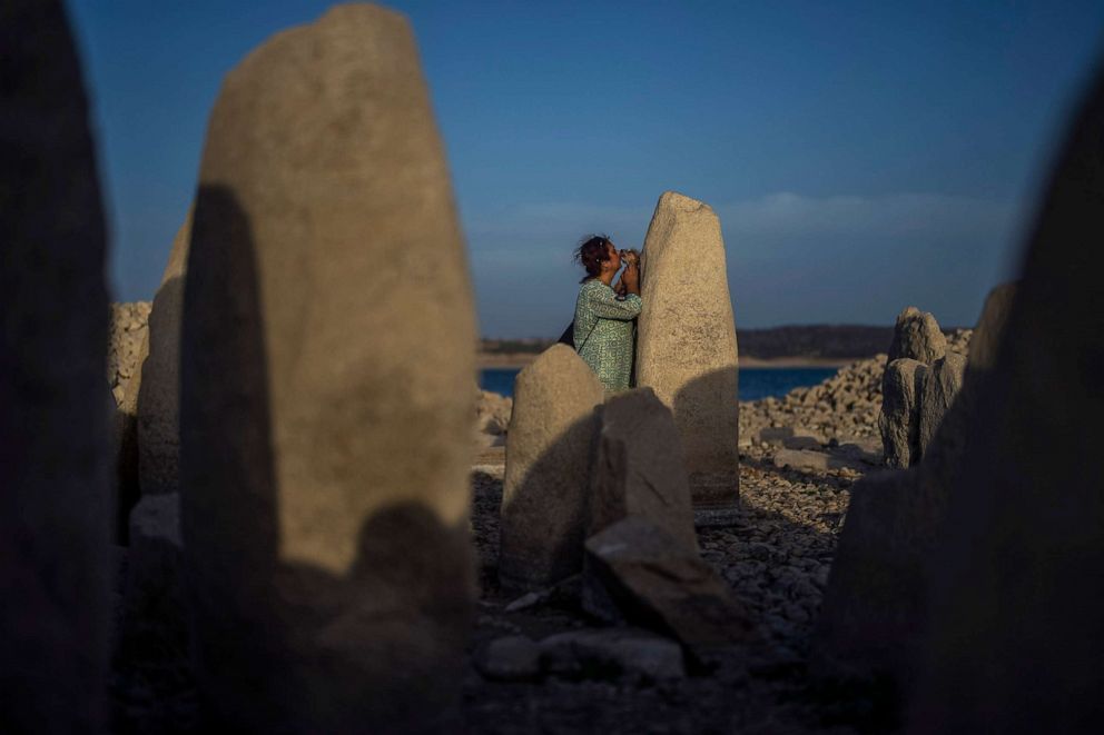 PHOTO: Amalie Garcia picks up her dog next to The Dolmen of Guadalperal, a megalithic monument that emerged due to drought at the Valdecanas reservoir in El Gordo, western Spain, Aug. 13, 2022.