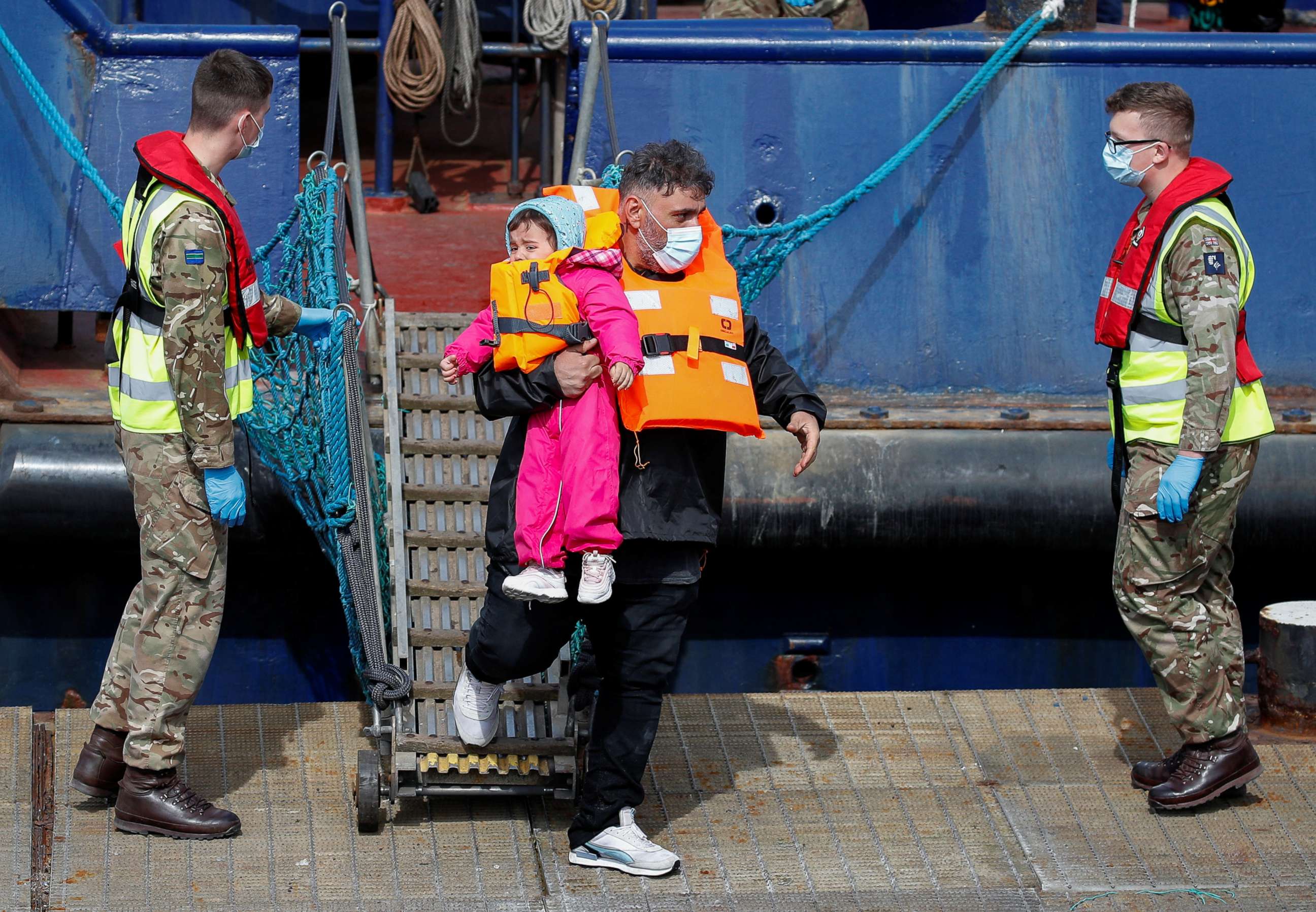 PHOTO: A migrant with a child walks past members of the British military as he arrives at the Port of Dover after being rescued while crossing the English Channel, in Dover, Britain, April 14, 2022.