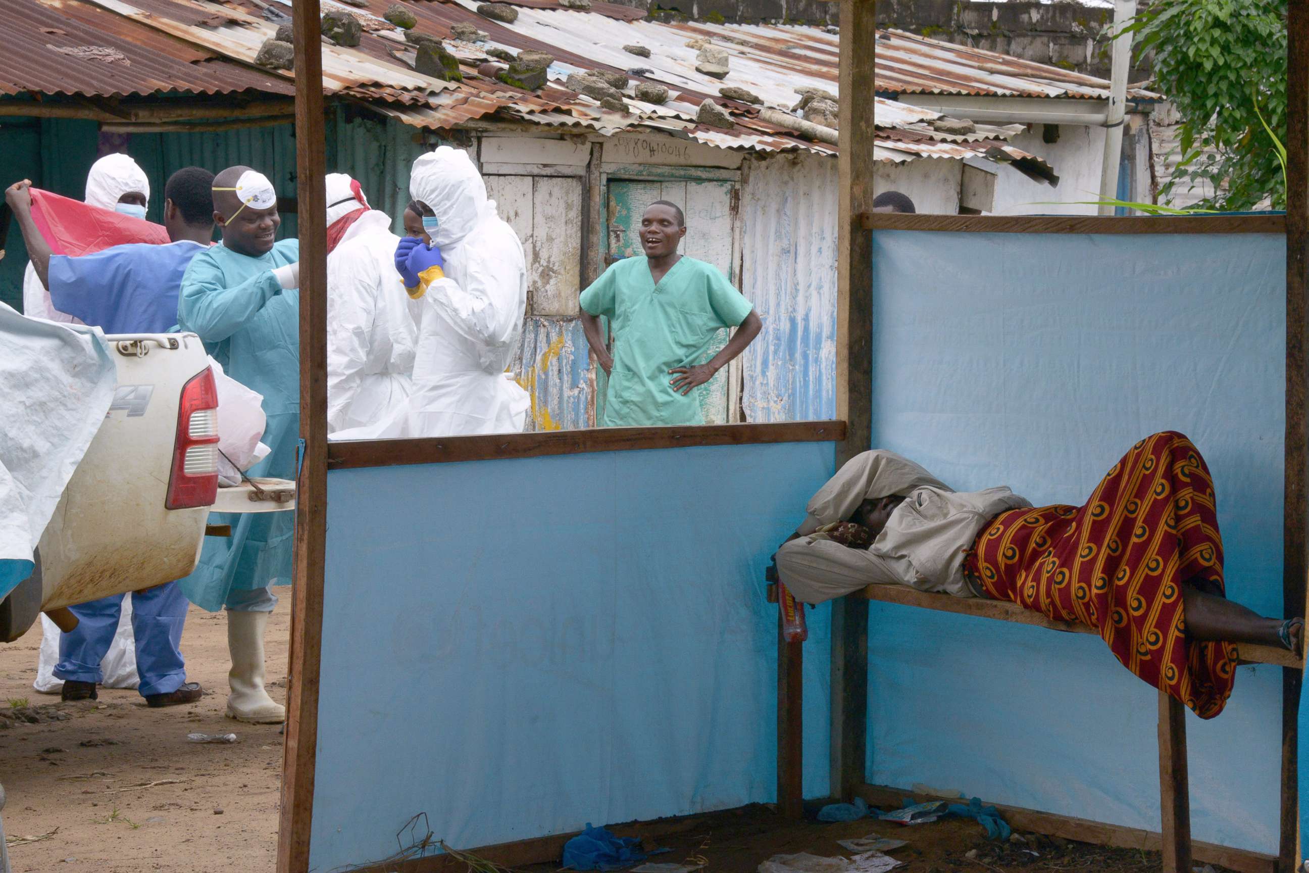 PHOTO: Medical workers of the John Fitzgerald Kennedy hospital in Monrovia, responsible for transport of the bodies of Ebola virus victims, wear their protective suits as they walk past a sick woman waiting for assistance, on Sept. 6, 2014.