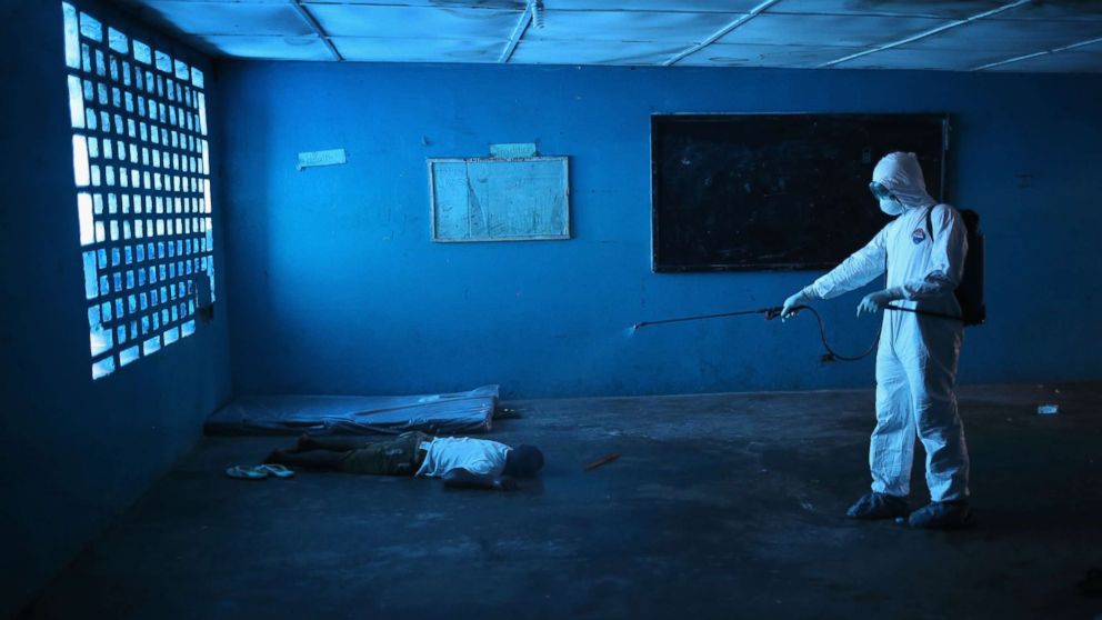 A Liberian health worker disinfects a corpse after the man died in a classroom now used as Ebola isolation ward on Aug. 15, 2014 in Monrovia, Liberia. 