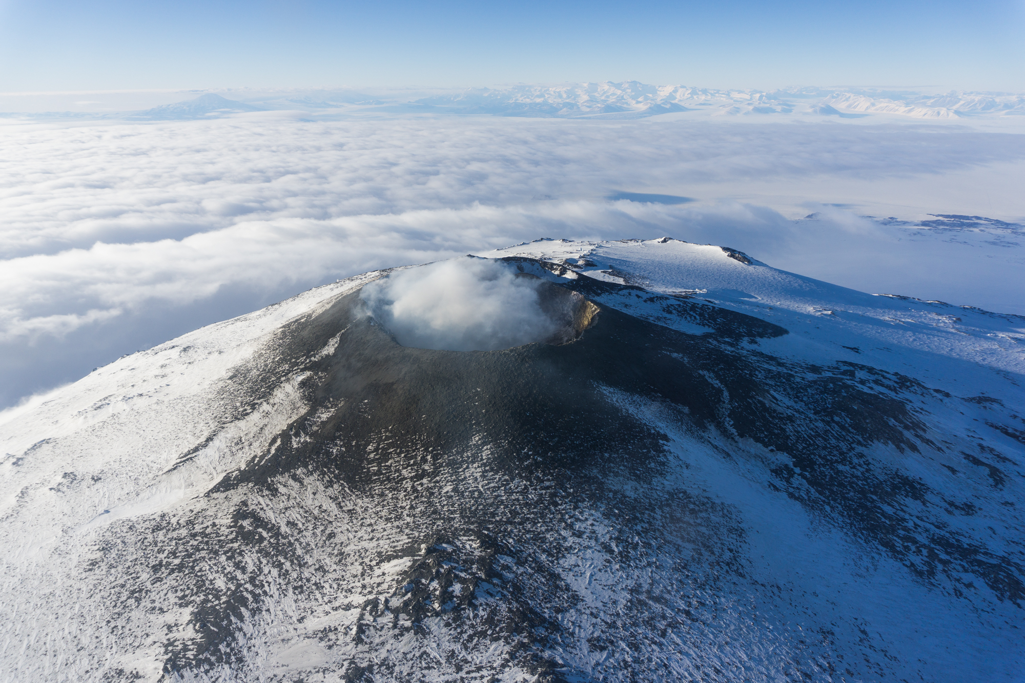 PHOTO: The crater of Mount Erebus is viewed from helicopter as steam is emitted from the molten lava lake a few hundred feet beneath the crater rim. In the background are the Transantarctic Mountains, one of the longest mountain chains in the world. 