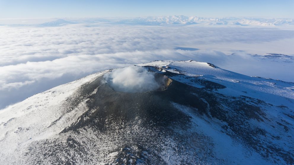 PHOTO: The crater of Mount Erebus is viewed from helicopter as steam is emitted from the molten lava lake a few hundred feet beneath the crater rim. In the background are the Transantarctic Mountains, one of the longest mountain chains in the world. 