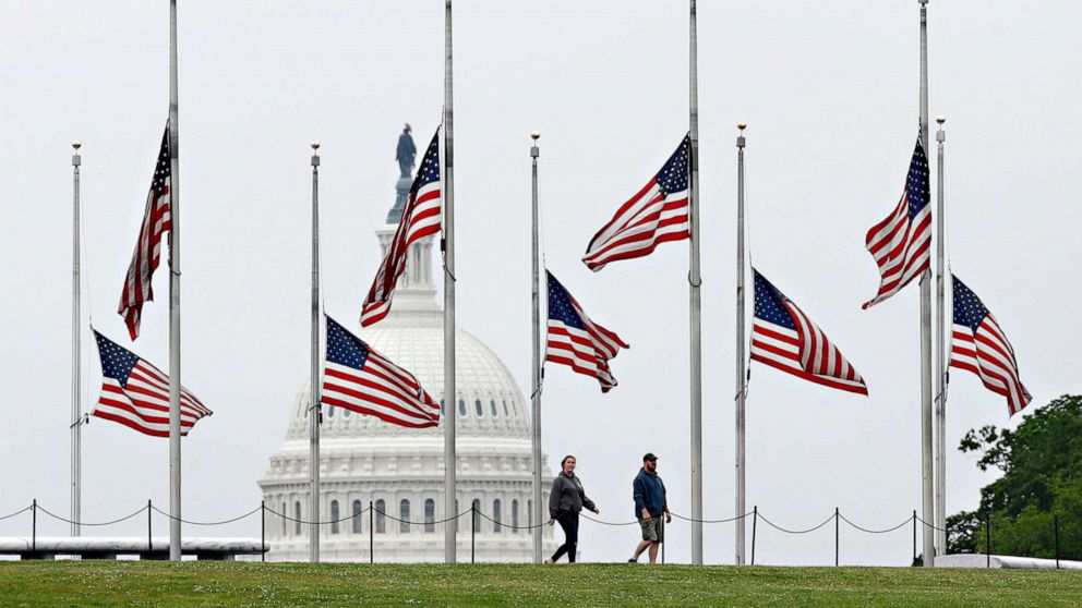 PHOTO: People walk past flags flying at half-staff at the Washington Monument, May 22, 2020, in Washington.