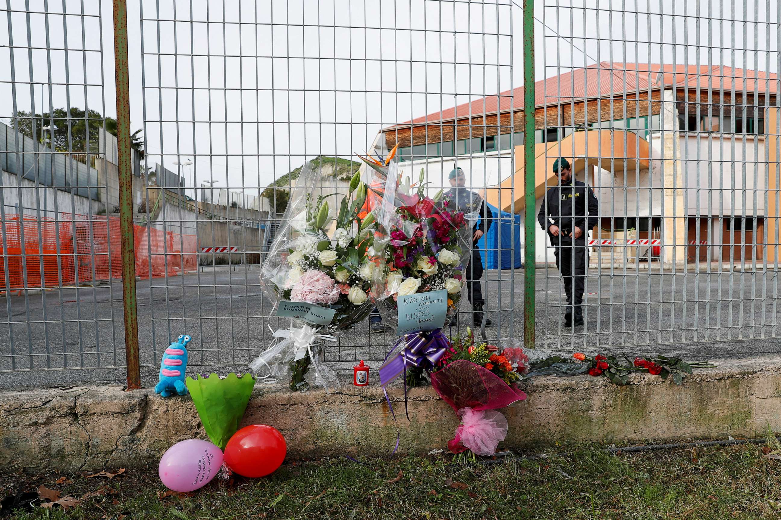 PHOTO: Members of the Guardia di Finanza stand next to floral tributes laid at the fence of PalaMilone sports hall, where victims of a deadly migrant shipwreck are being held, in Crotone, Italy, Feb. 27, 2023.