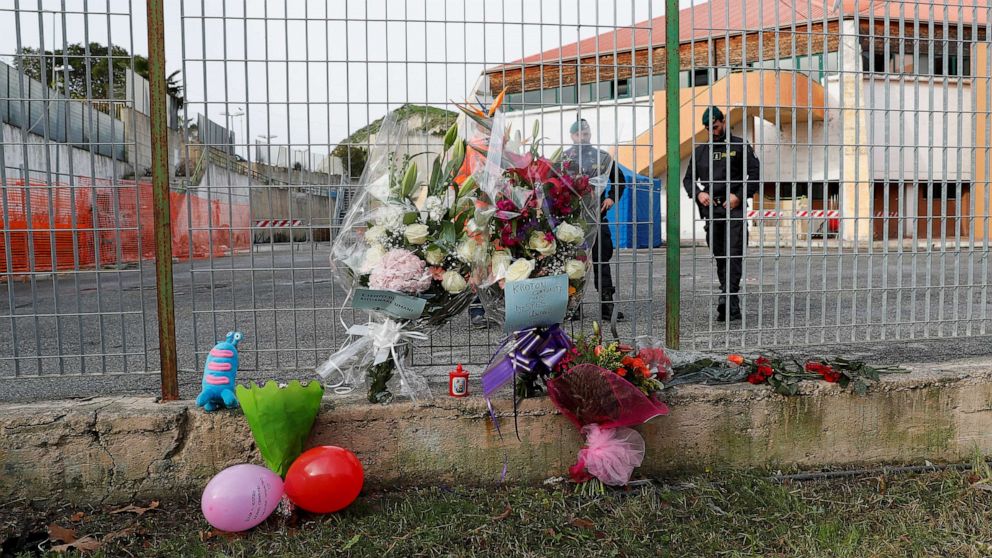 PHOTO: Members of the Guardia di Finanza stand next to floral tributes laid at the fence of PalaMilone sports hall, where victims of a deadly migrant shipwreck are being held, in Crotone, Italy, Feb. 27, 2023.
