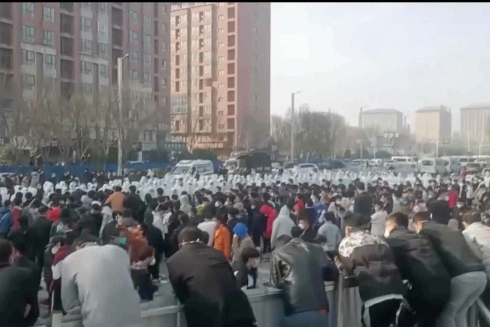 عکس فایل: معترضان با پرسنل امنیتی با لباس‌های محافظ سفید در کارخانه‌ای که توسط گروه فناوری فاکس‌کان اداره می‌شود، که بزرگترین کارخانه آیفون اپل در جهان را اداره می‌کند، در ژنگژو، استان هنان مرکز چین، مواجه می‌شوند.  چین
