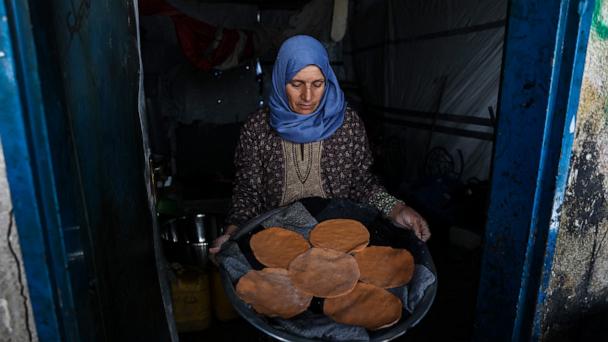A Palestinian woman carries flat bread made with ground lentils during a flour shortage, in her shelter in the Jabalia camp for refugees in the northern Gaza Strip, May 6, 2025. 