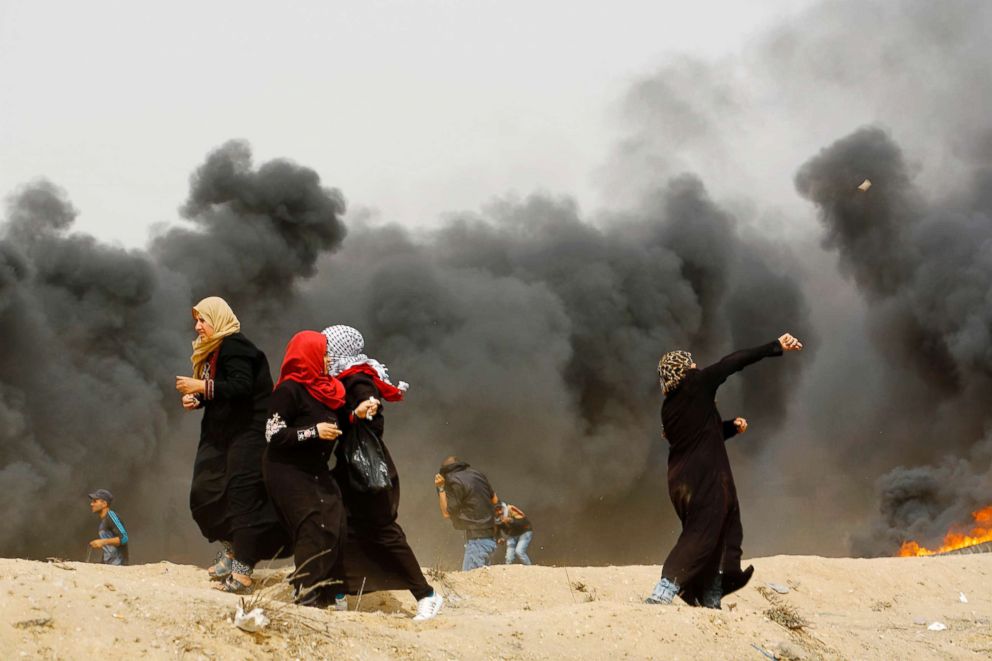 PHOTO: Palestinian women throw stones past smoke plume rising from burning tires during clashes with Israeli forces across the border on April 20, 2018.