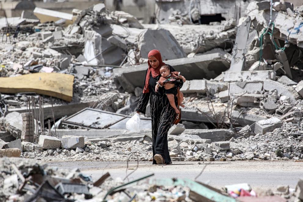 PHOTO: A woman walks with an infant past the rubble of a collapsed building in Khan Yunis in the southern Gaza Strip on September 16, 2024 amid the ongoing war in the Palestinian territory between Israel and Hamas.