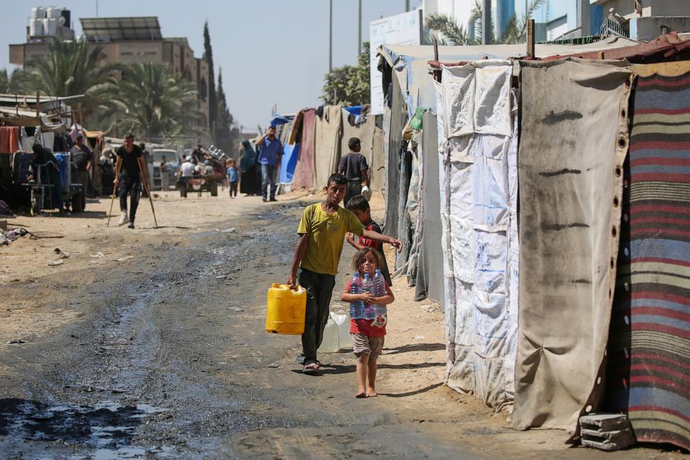 PHOTO: Displaced Palestinian children haul water to their tent in a makeshift camp in the perimeter of the Al-Aqsa Martyrs Hospital in Deir al-Balah in the central Gaza Strip following renewed Israeli evacuation orders for the area on Aug. 26, 2024.