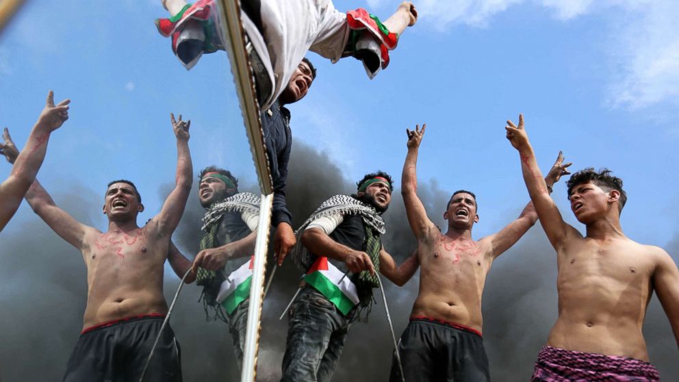 Palestinian protesters use a reflective mirror to divert the attention of members of the Israeli forces during a tent city protest at the Israel-Gaza border, in Khan Yunis in the southern Gaza Strip, April 2, 2018.