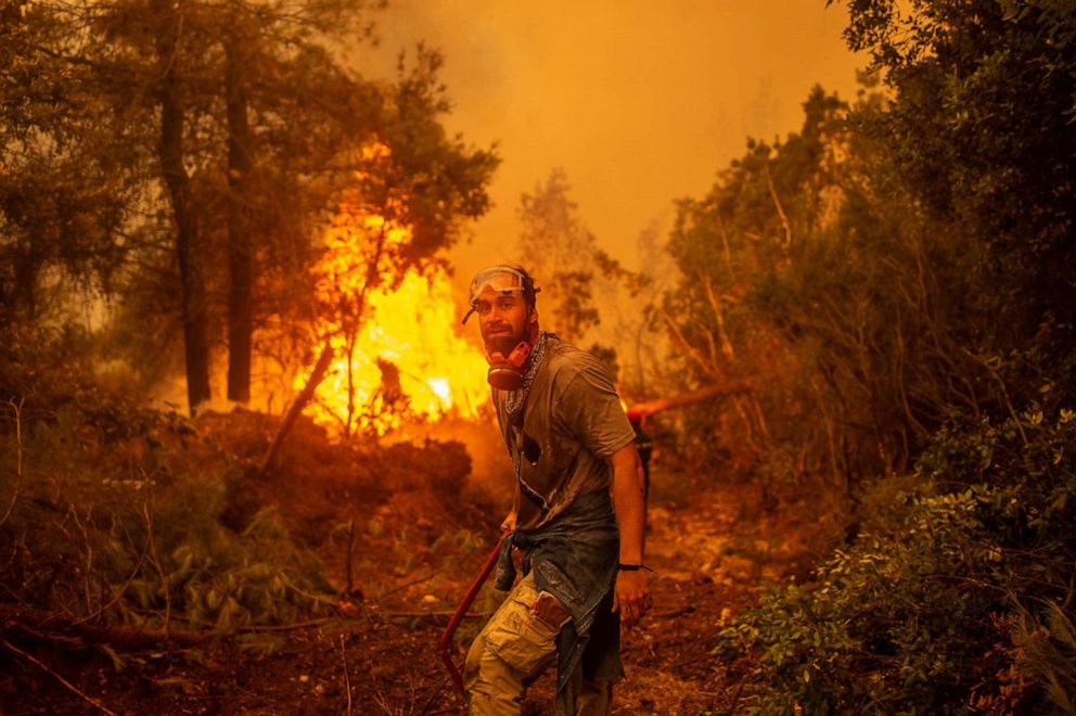 PHOTO: A volunteers holds a water hose near a burning blaze as he tries to extinguish a fire in the village of Glatsona on Evia island, on August 9, 2021.