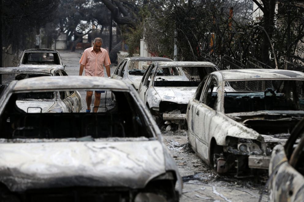 A man passes burned cars in Mati, east of Athens, Tuesday, July 24.
