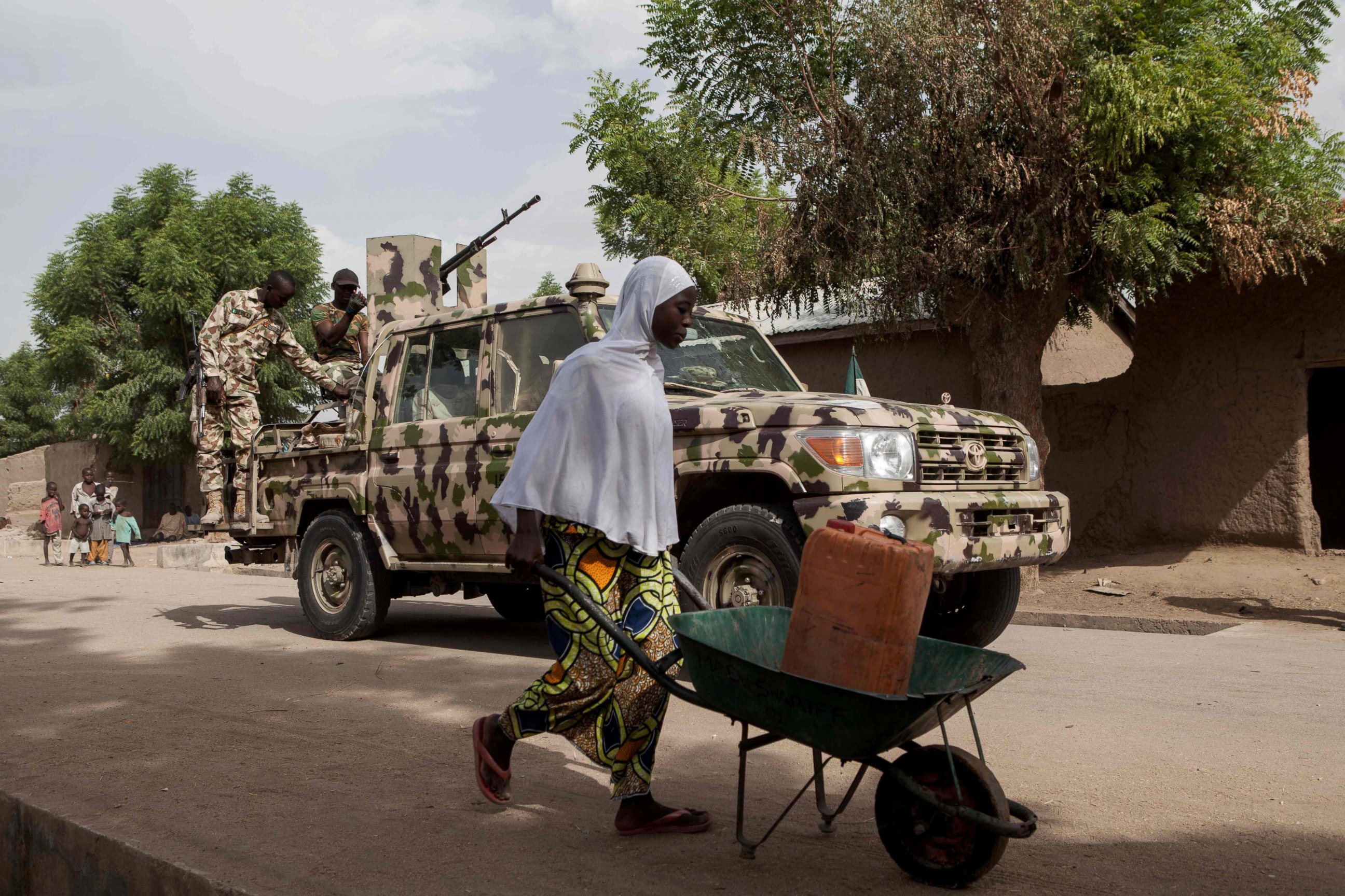 PHOTO: A woman pushes a wheelbarrow carrying a jerrycan filled with water as Nigerian soldiers patrol in the town of Banki in northeastern Nigeria, April 26, 2017. 
