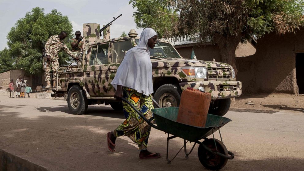 PHOTO: A woman pushes a wheelbarrow carrying a jerrycan filled with water as Nigerian soldiers patrol in the town of Banki in northeastern Nigeria, April 26, 2017. 