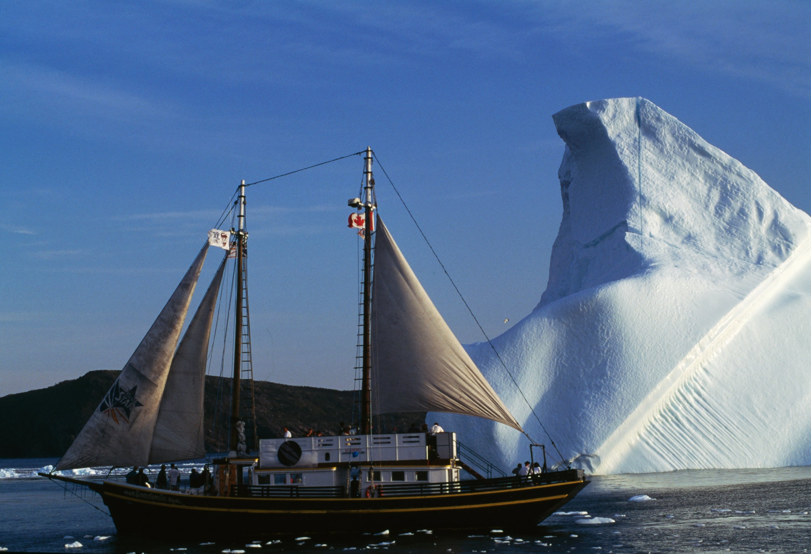 PHOTO: A Sailboat in front of an iceberg, in Saint Bay, Newfoundland, Canada. 